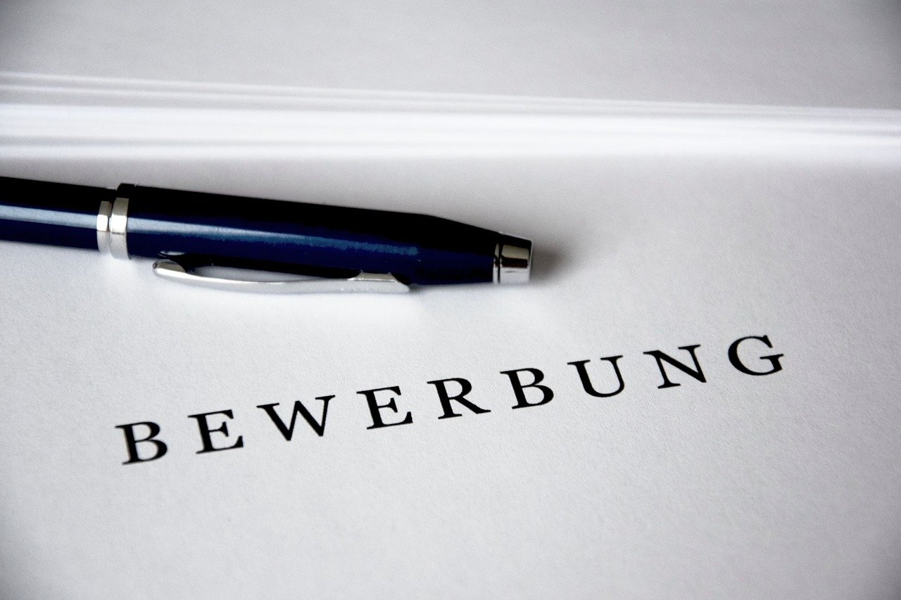 Das Bild zeigt einen Stift und ein Blatt Papier. Das Papier trägt den Aufdruck BEWERBUNG