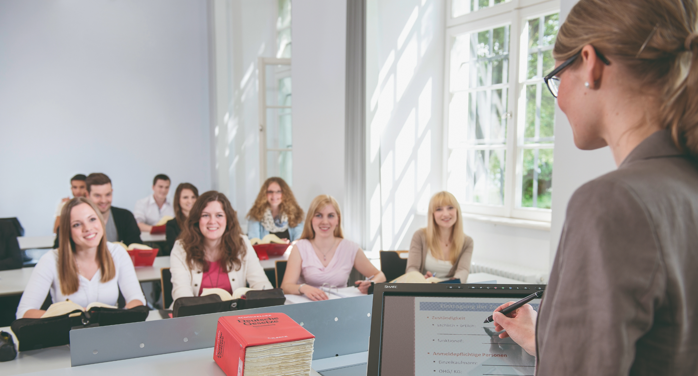 Dozentin, die in Hörsaal vor Studierenden am SMART-Podium steht.