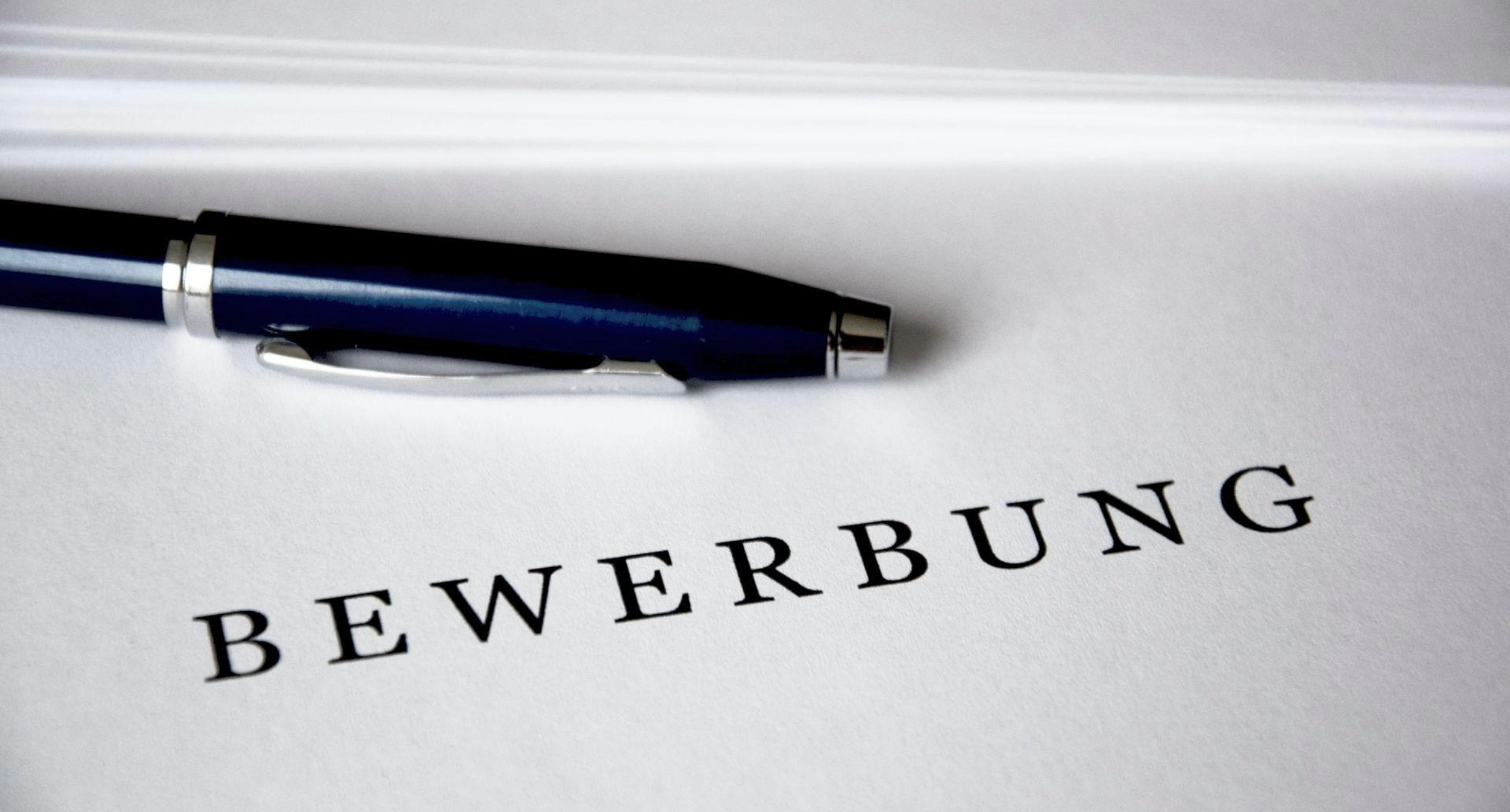 Schwarzer Stift und ein Blatt Papier. Das Papier trägt den Aufdruck Bewerbung