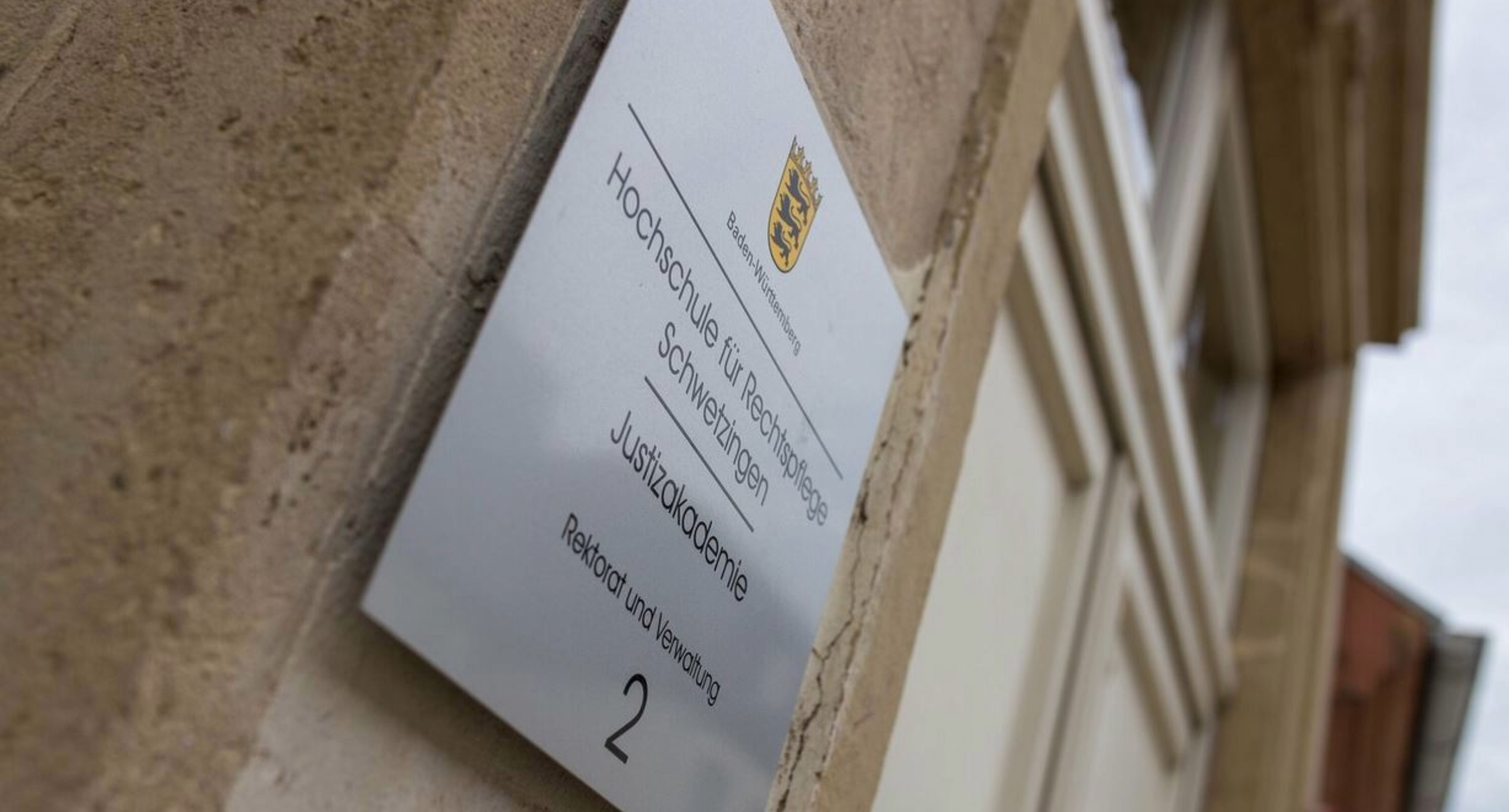 Bild zeigt ein Schild an einem Gebäude. Das Schild trägt die Aufschrift Hochschule für Rechtspflege Schwetzingen Justizakademie Rektorat und Verwaltung