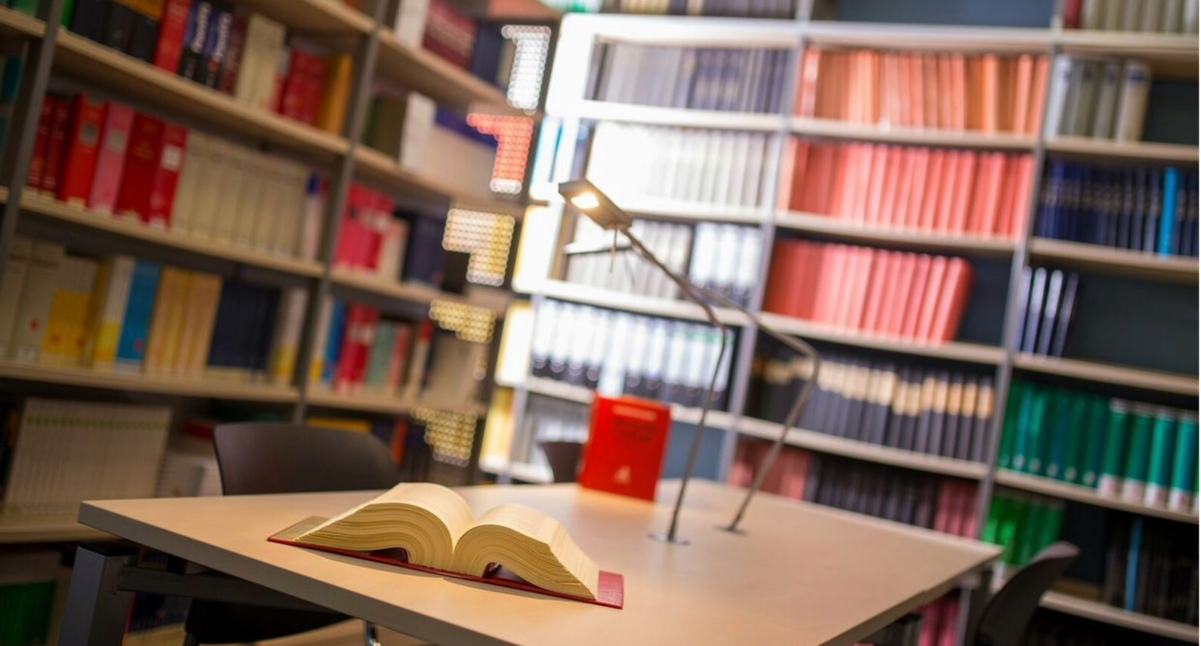 Tisch und Bücherregale. Auf dem Tisch liegt ein aufgeschlagenes Buch.